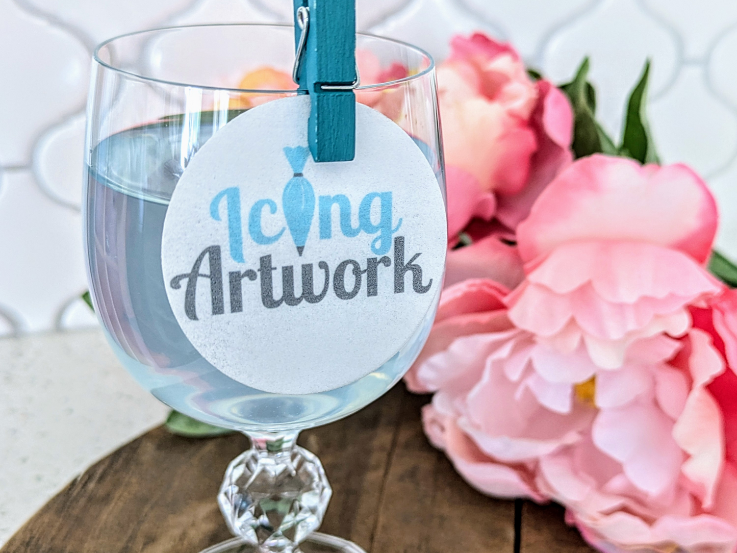 Wine glass with 'Icing Artwork' tag and pink flowers in the background