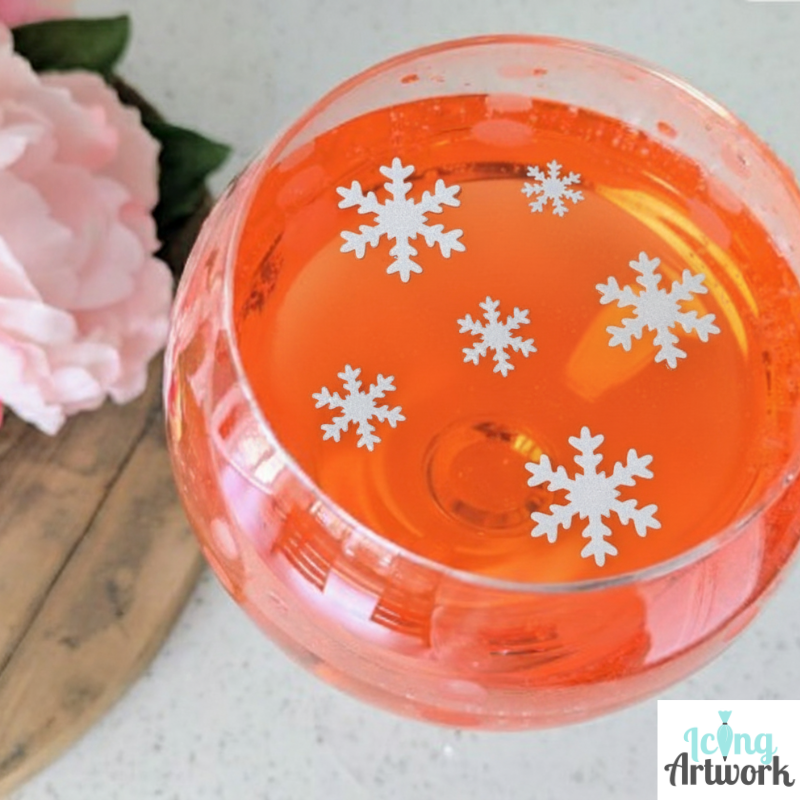 Edible pre-cut wafer paper snowflake drink toppers, next to pink flowers.