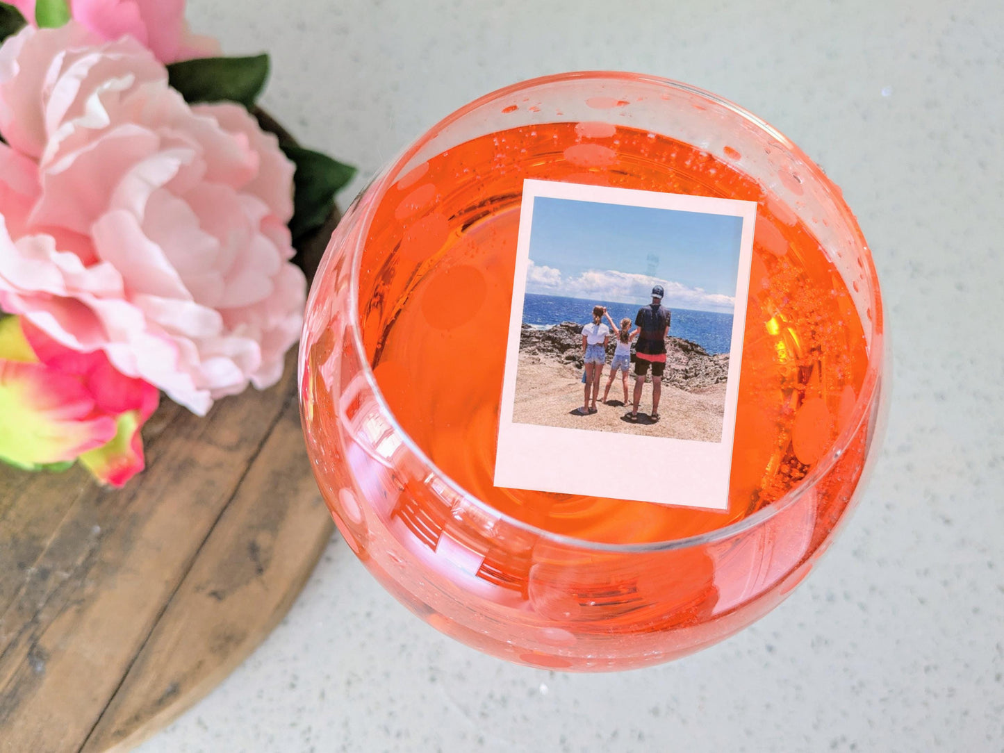 Edible Cocktail garnish topper with a photo of people by the ocean, surrounded by pink flowers on a wooden surface.