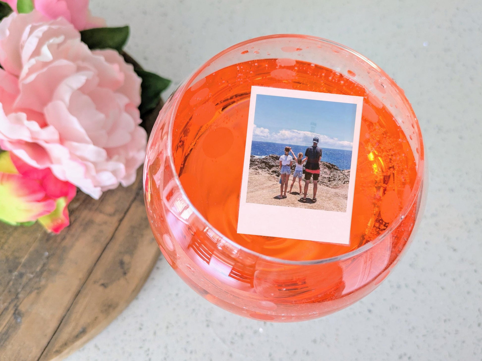 Edible Cocktail garnish topper with a photo of people by the ocean, surrounded by pink flowers on a wooden surface.