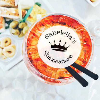 Clear plastic cup with orange design and 'Gabriella's Quinceanera' text, surrounded by snacks on a white surface.