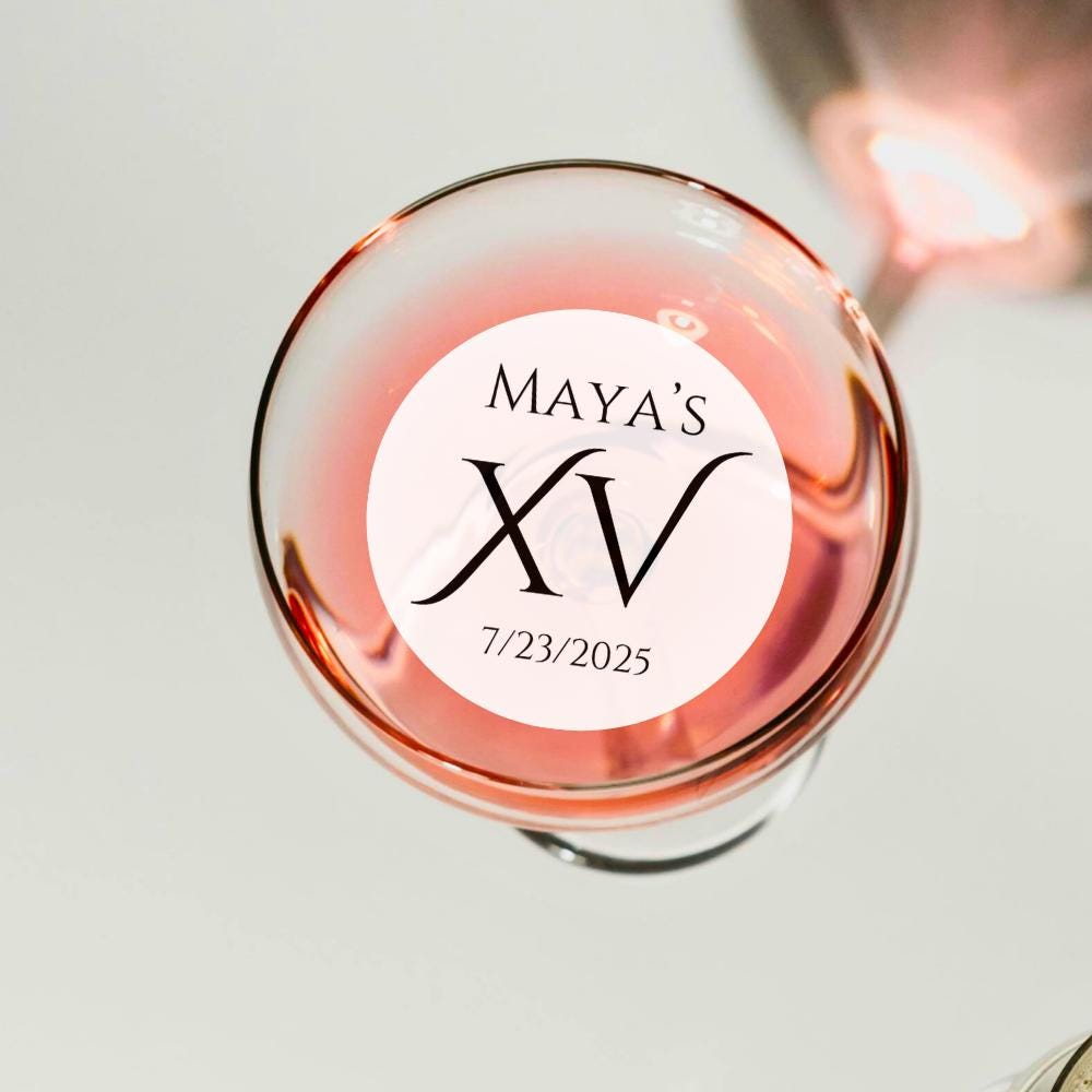 Glass of pink wine with a 'Maya's XV' edible drink topper on a light background