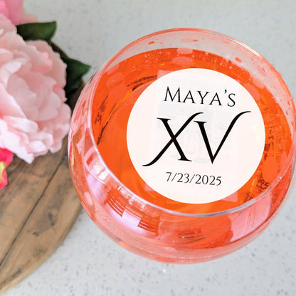 Custom birthday drink toppers with 'MAYA'S XV 7/23/2025' garnish next to pink flowers on a wooden surface.