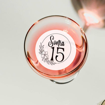 Glass of pink wine with a decorative cocktail garnish topper label on a light background