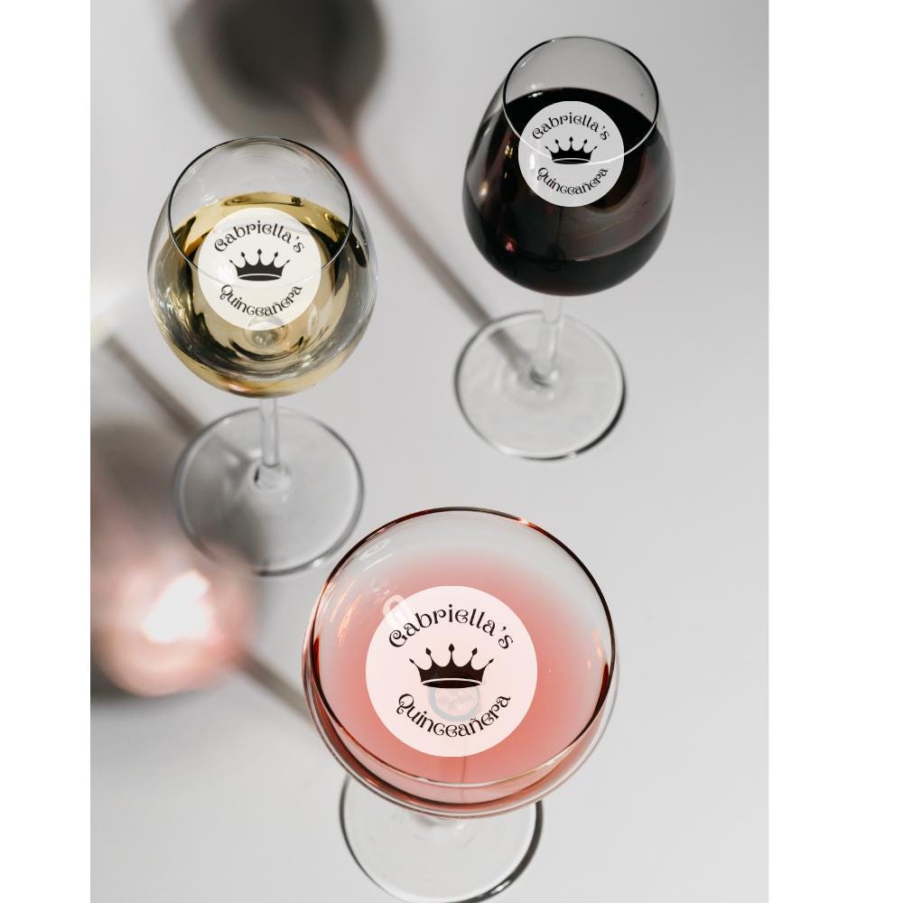 Three wine glasses with edible drink garnish 'Gabriella's Quinceañera' labels on a light gray background