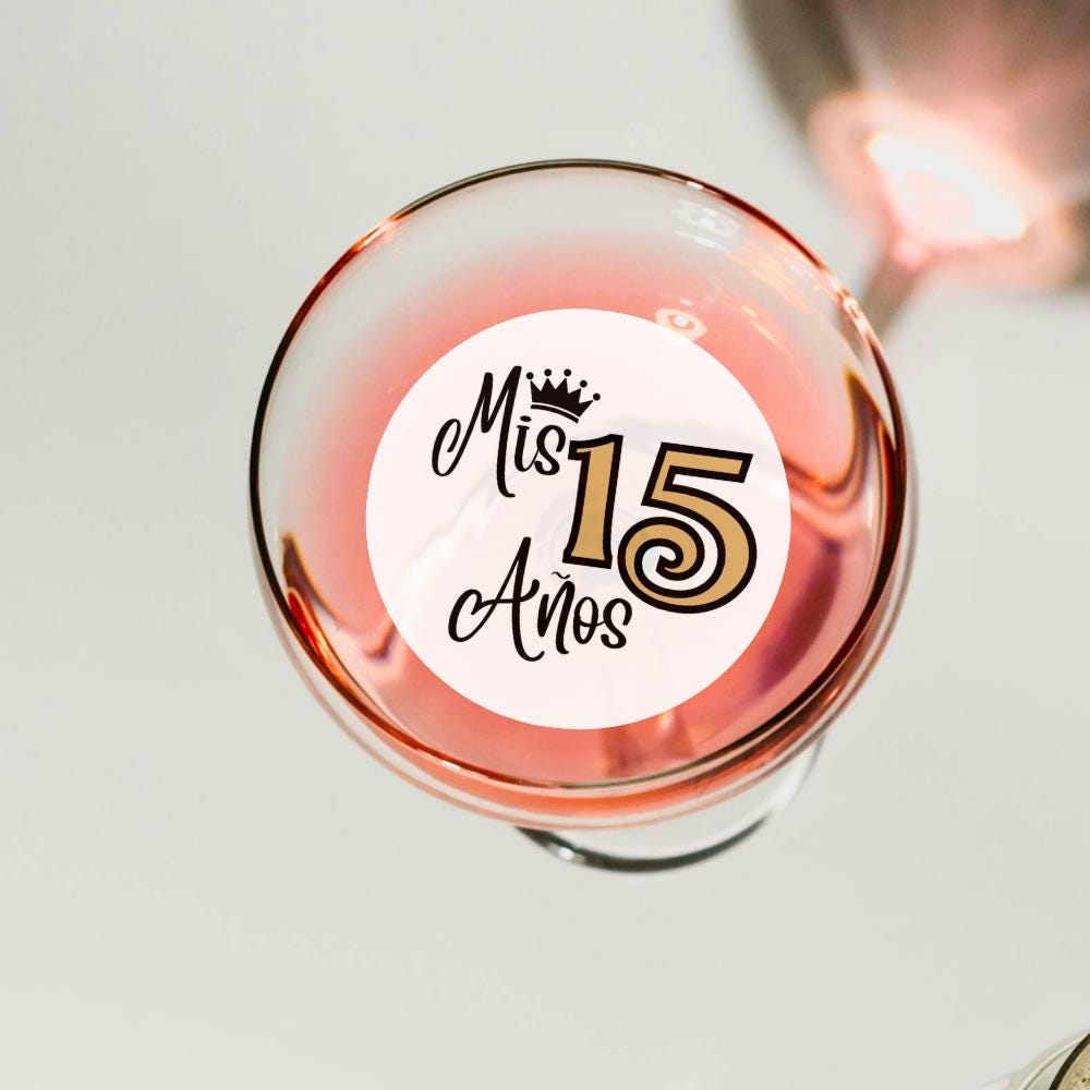 Glass of pink wine with a 'Mis 15 Años' edible drink topper on a light background