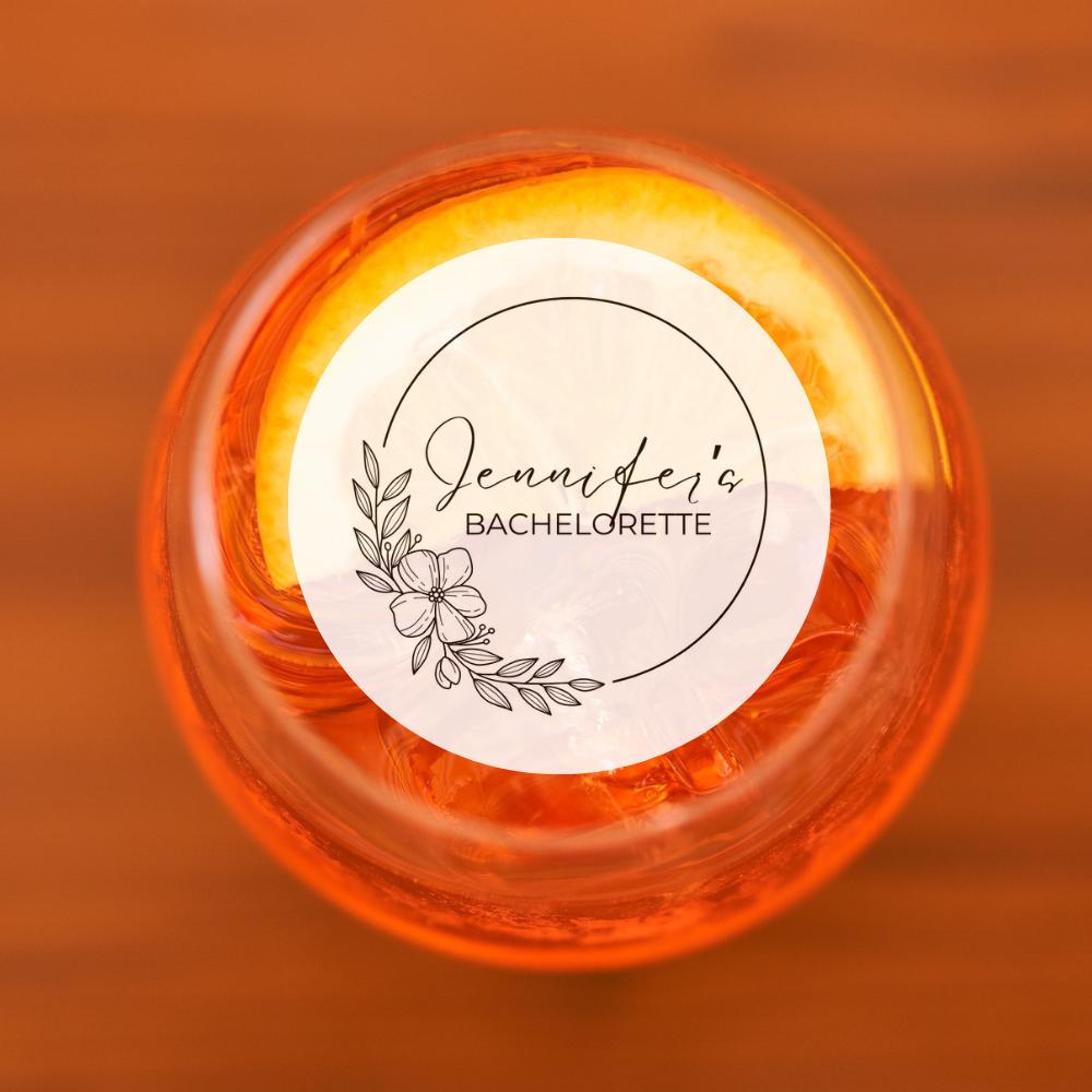 Round cocktail garnish with 'Jennifer's Bachelorette' text on a blurred orange background