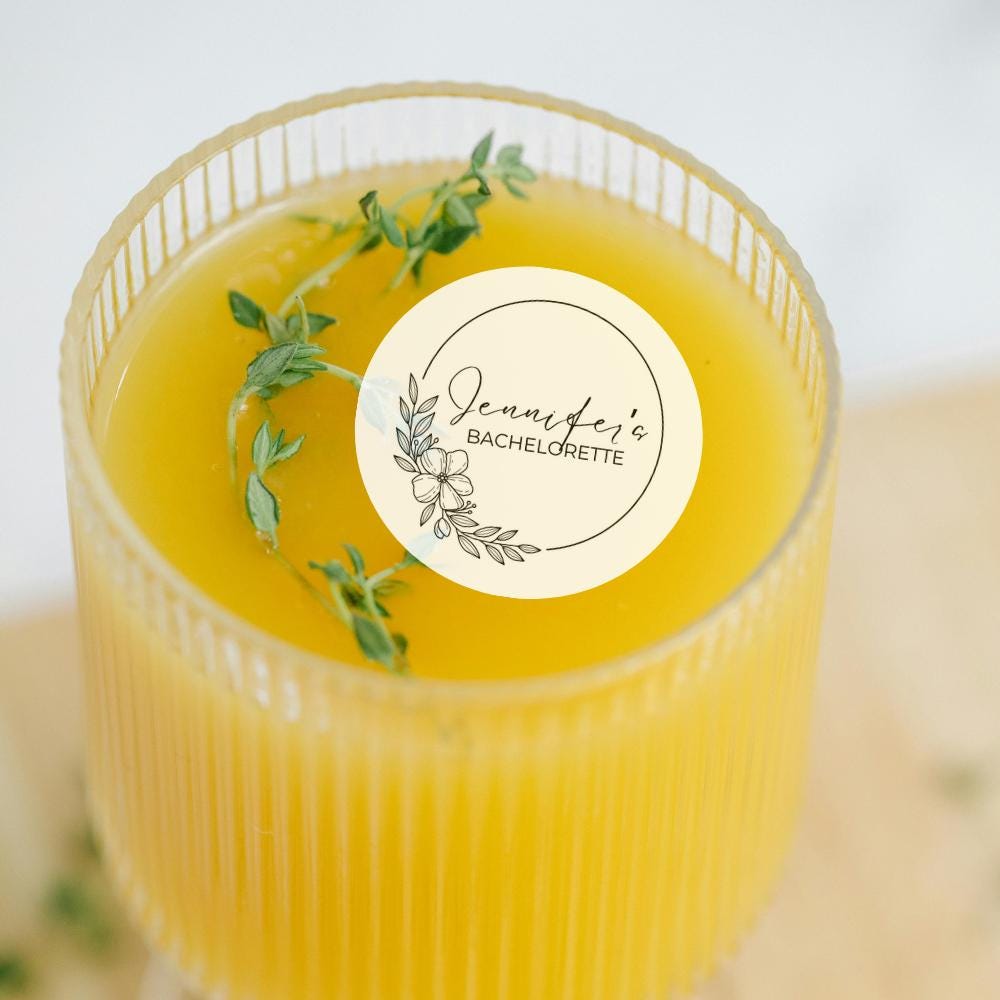 Glass of yellow liquid with a custom edible cocktail garnish on a light background