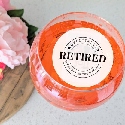 Orange cocktail with a 'Officially Retired' edible image drink topper next to pink flowers on a light surface