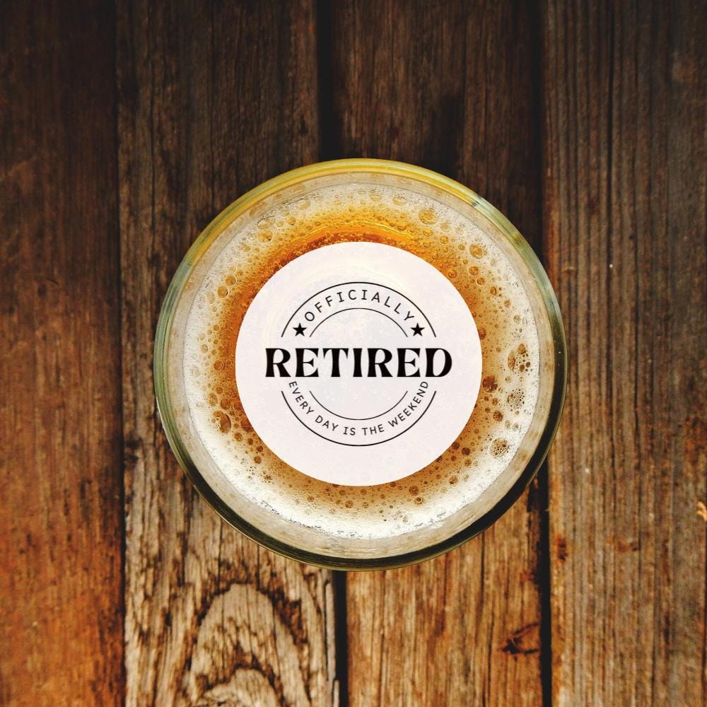 Glass of beer with a 'Officially Retired' custom drink topper on a wooden surface