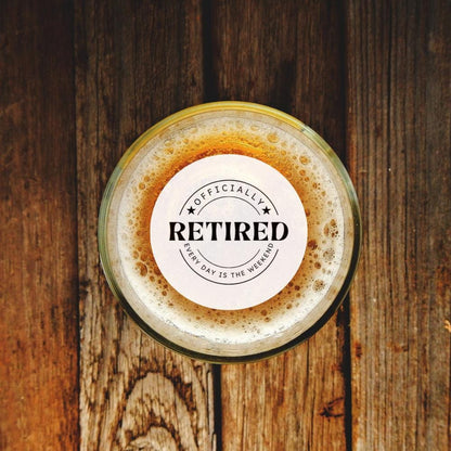Glass of beer with a 'Officially Retired' custom drink topper on a wooden surface