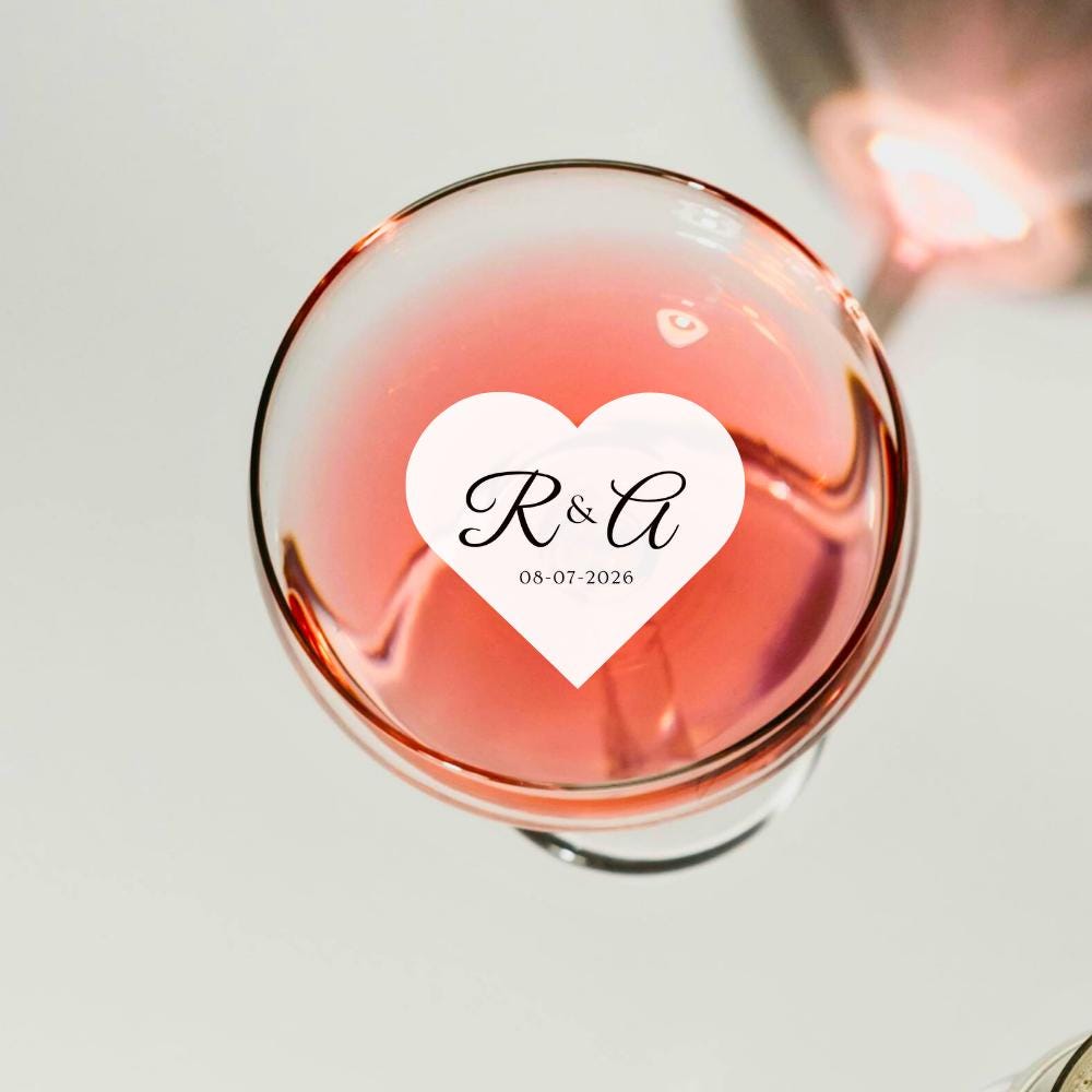 Glass of pink wine with a heart-shaped edible topper featuring initials and date on a light background