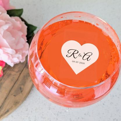 Clear glass bowl with a custom  heart-shaped edible drink sticker featuring initials and date, surrounded by pink flowers.