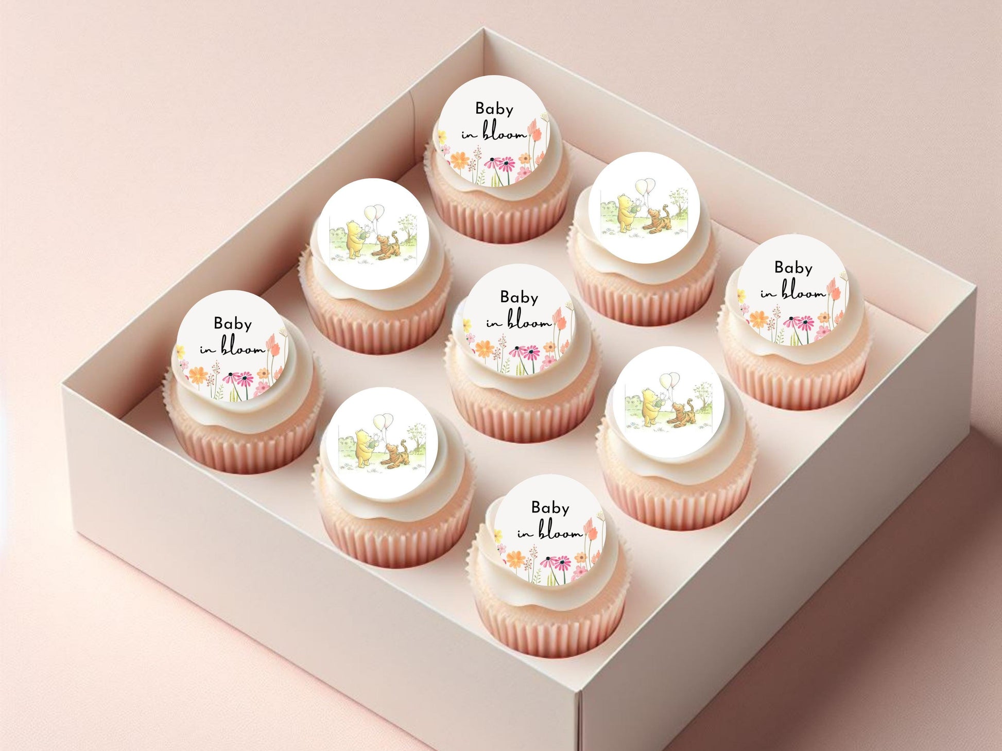 Box of cupcakes with 'Baby in Bloom' decorations on a light pink background